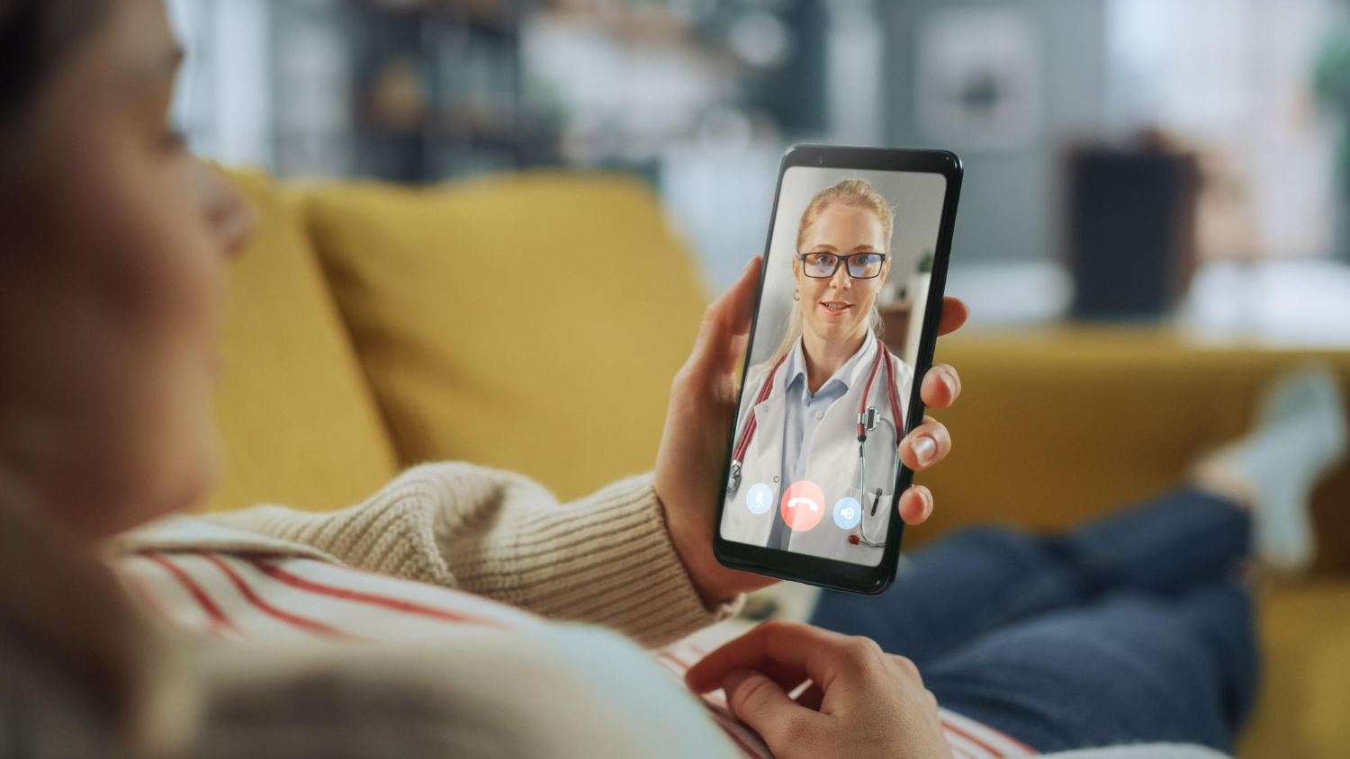 Person lying on a couch having a video call with a doctor on their smartphone.