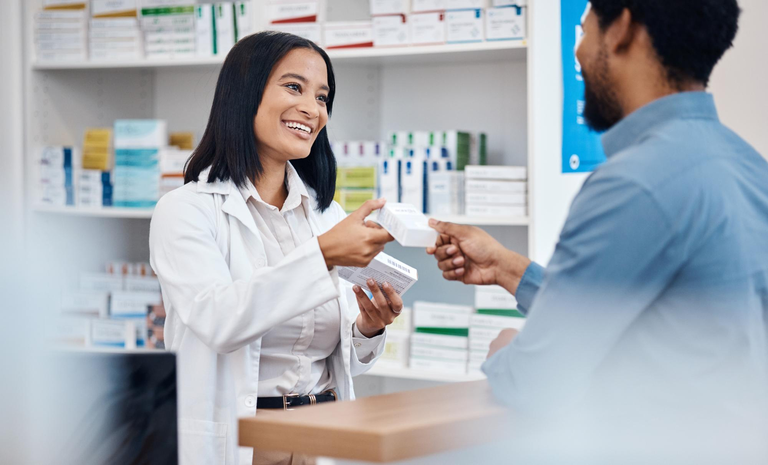 A pharmacist hands a medication box to a smiling customer at a pharmacy counter.