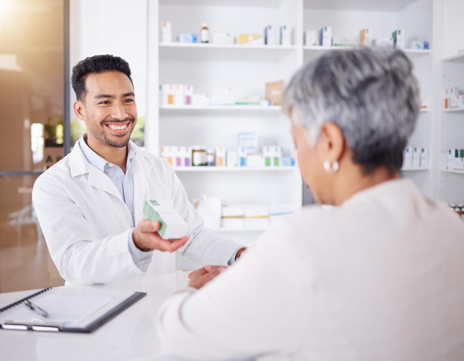 Smiling pharmacist hands medication to a customer across the counter in a pharmacy.
