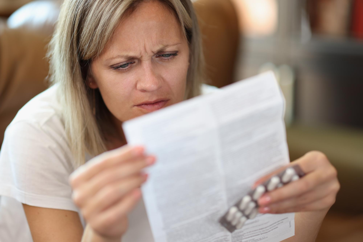 A woman frowns while reading a medication leaflet and holding a blister pack of pills.