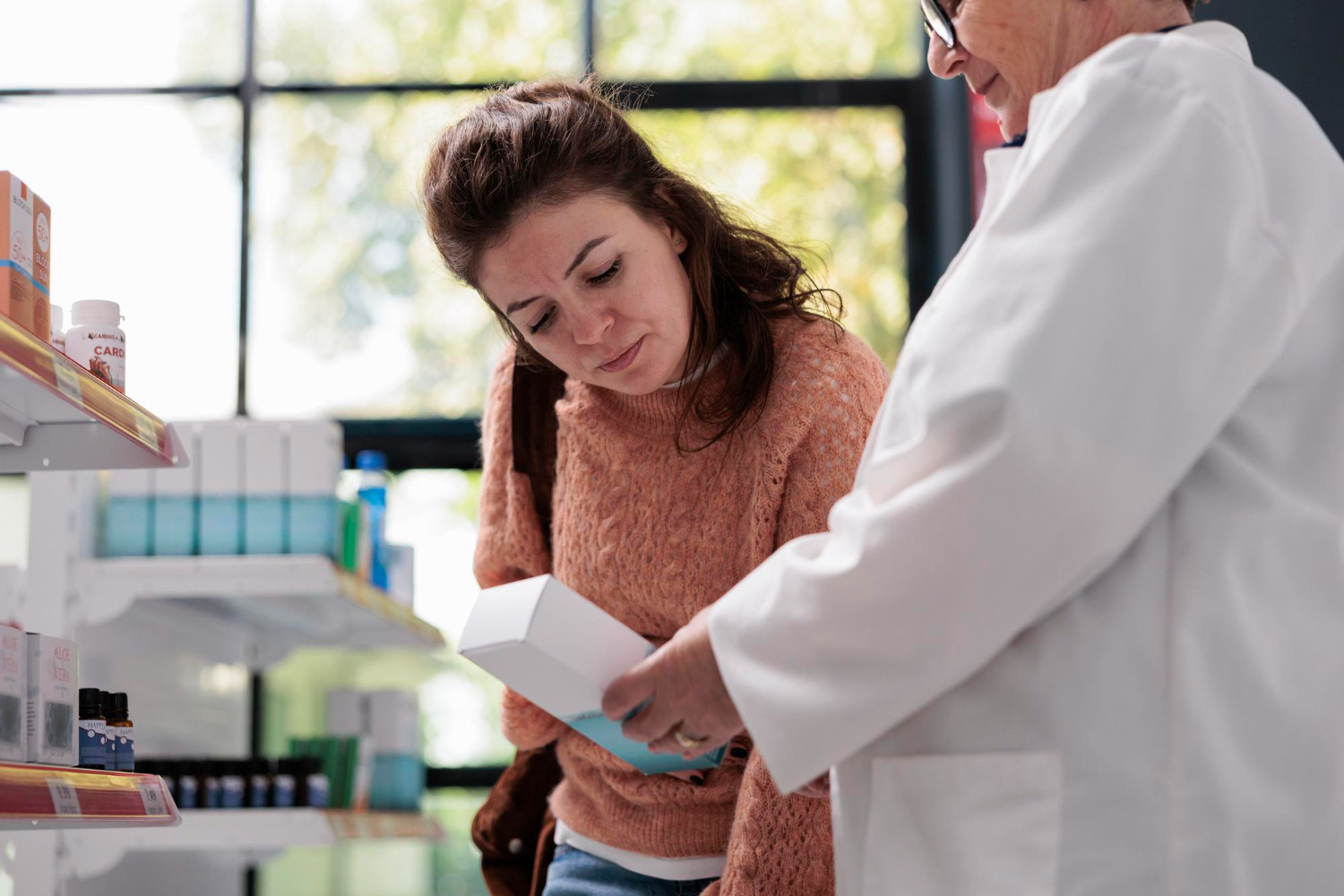 A woman and a pharmacist examine a product box together in a pharmacy.