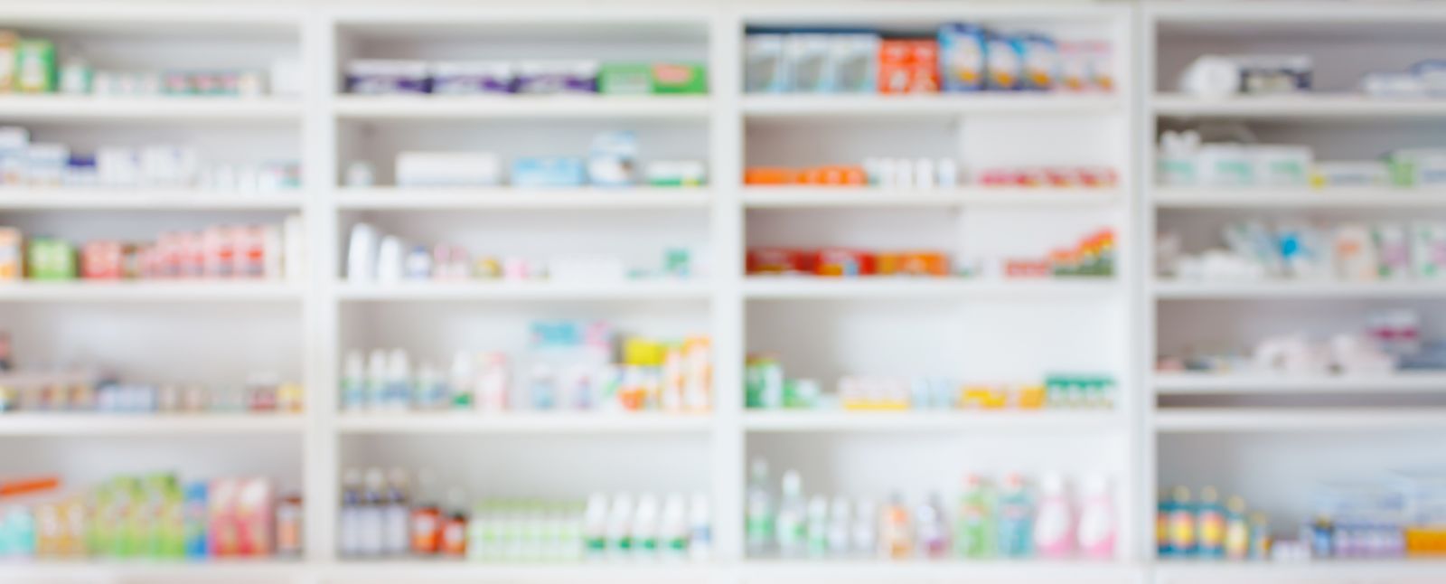 Blurred shelves filled with various medicines and health products in a pharmacy or drugstore.
