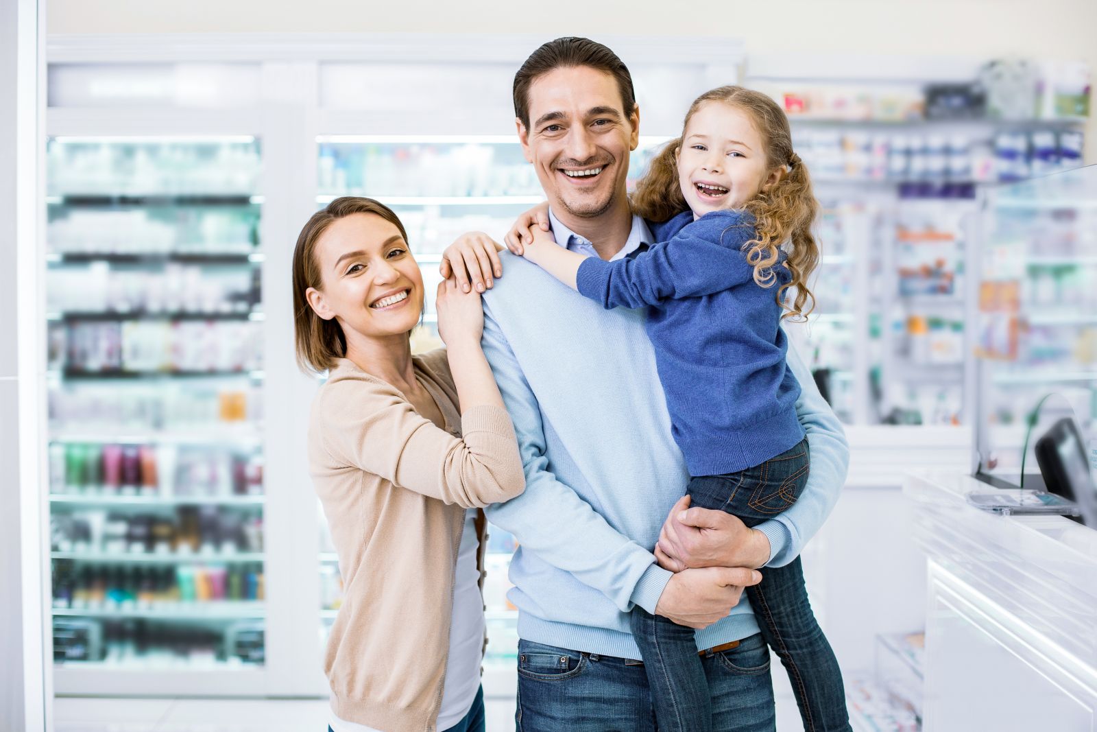 Smiling family with a young girl standing together in a bright pharmacy or drugstore.