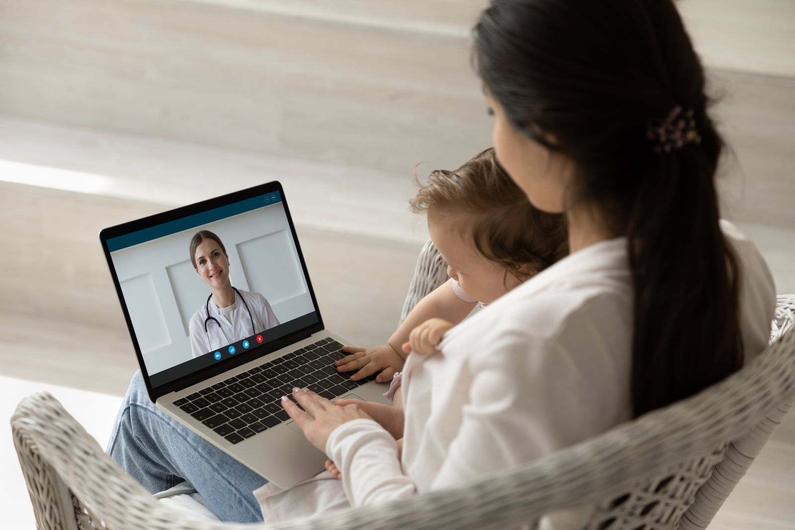 Woman with a child on her lap has a video call with a doctor on a laptop.