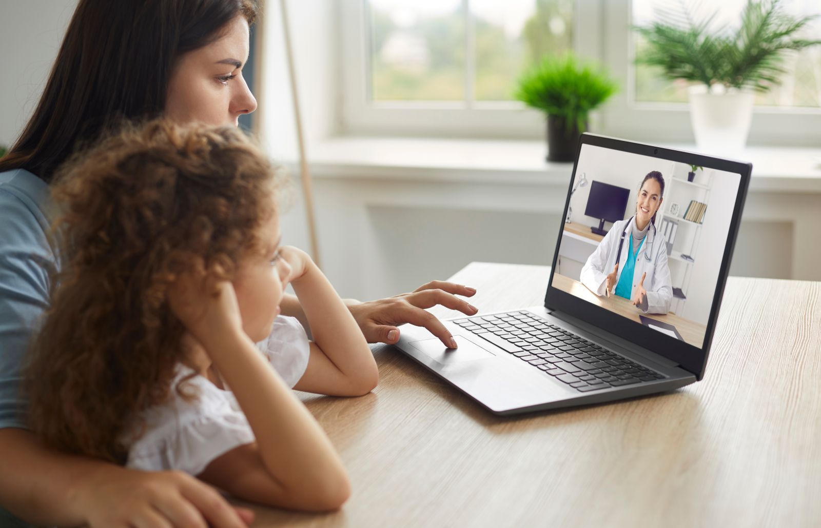 A woman and child have a video call with a doctor on a laptop at home.