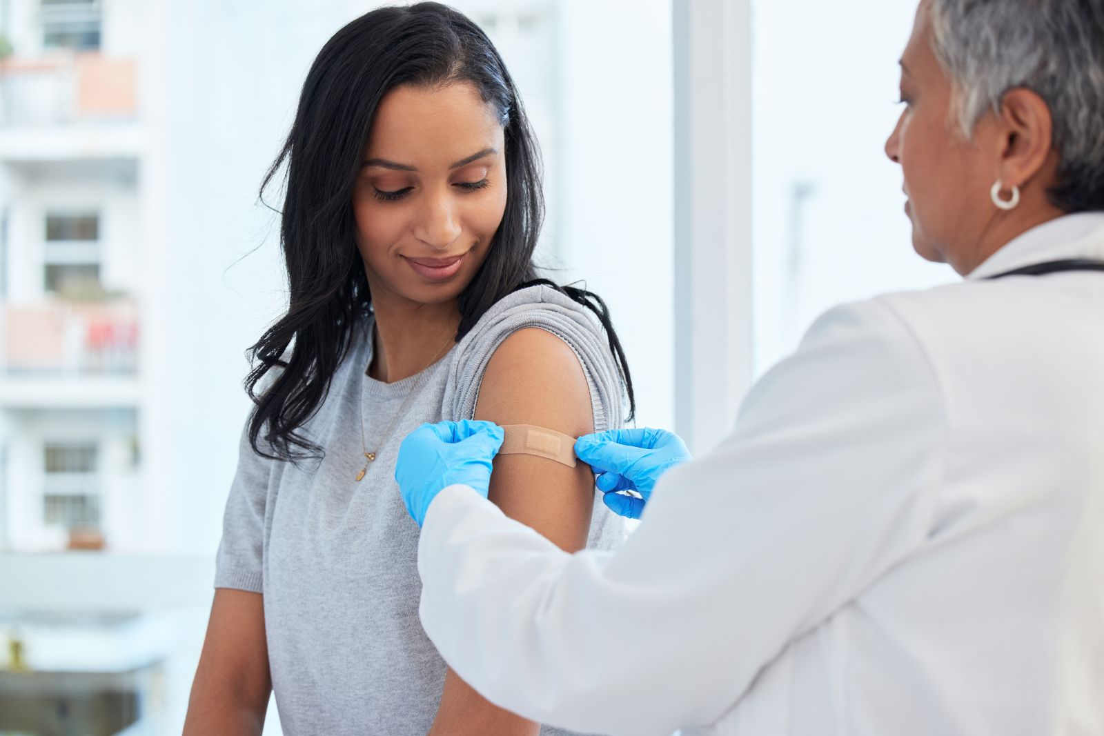 A doctor applies a bandage to a woman's arm after a vaccination in a bright room.
