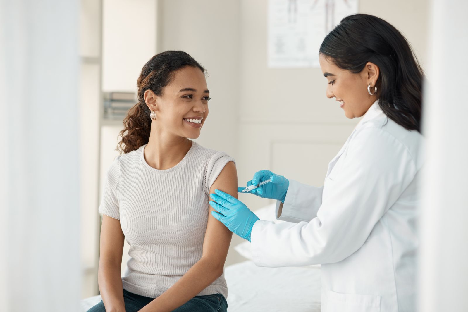 Smiling woman receives a vaccine injection in her arm from a healthcare professional wearing gloves.