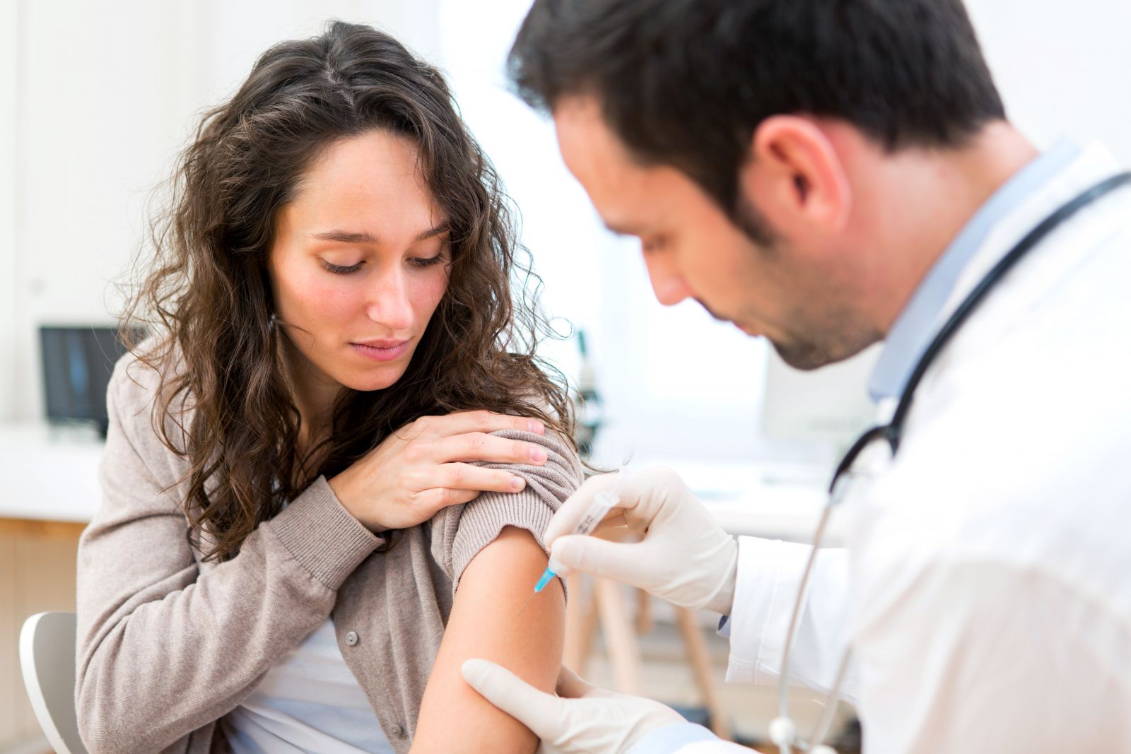 A doctor gives a woman an injection in her upper arm; she looks at the spot where the needle goes in.