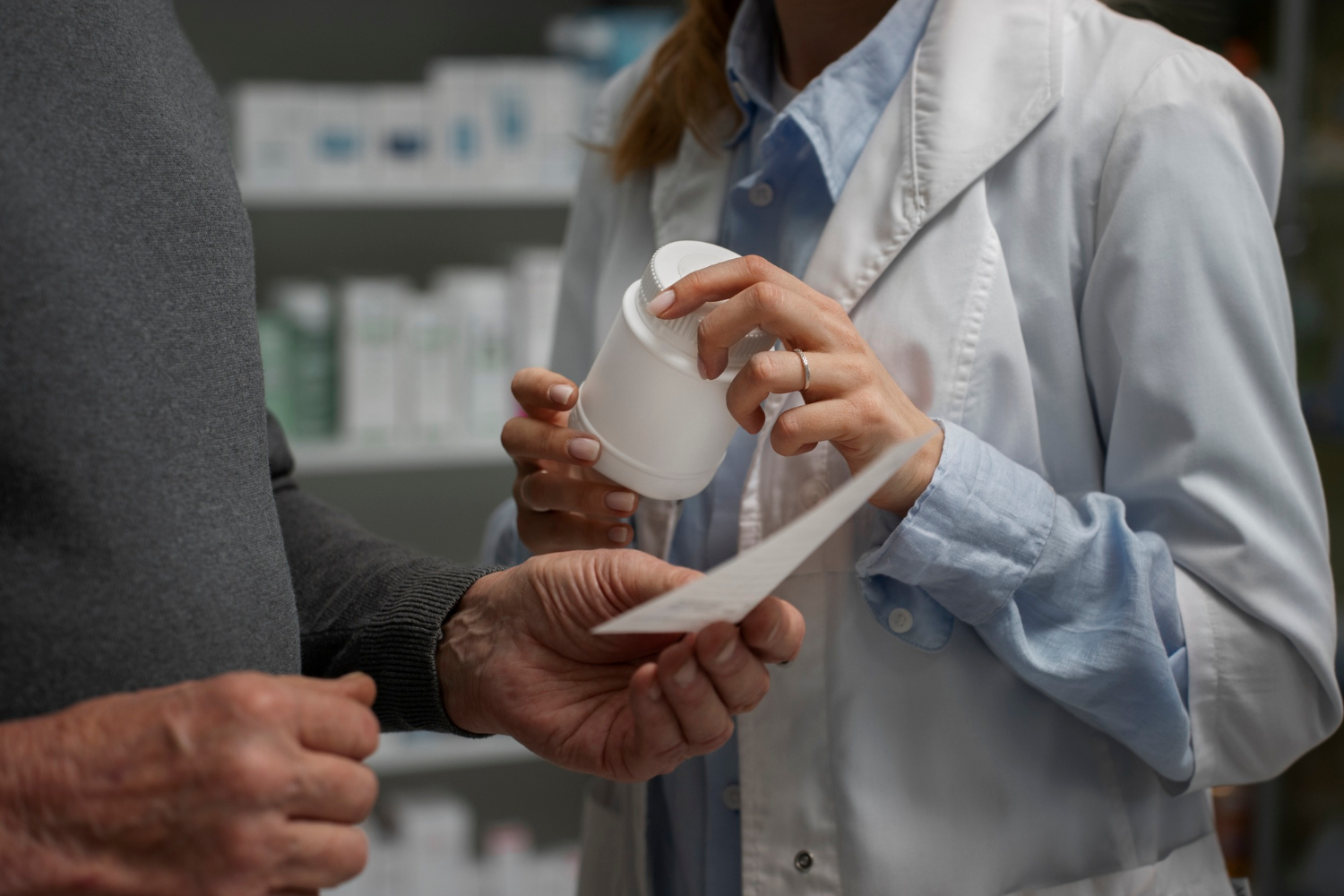 Pharmacist hands a prescription bottle to a customer while reviewing a prescription slip.